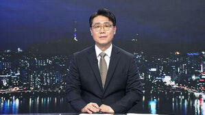 안경을 쓴 남성 뉴스 앵커가 야경을 배경으로 스튜디오 데스크에 앉아 있다.