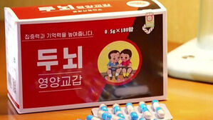 두뇌 영양교갑, 집중력과 기억력을 높여줍니다, 0.5g 곱하기 180알, 어린이 그림이 그려진 상자와 알약.