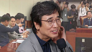 유시민 작가가 마이크를 잡고 있고 뒤편으로 국회 회의장 모습이 보임.