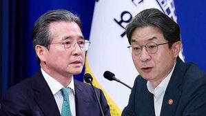안경을 쓴 두 남성이 나란히 서서 마이크를 앞에 두고 발언하는 모습