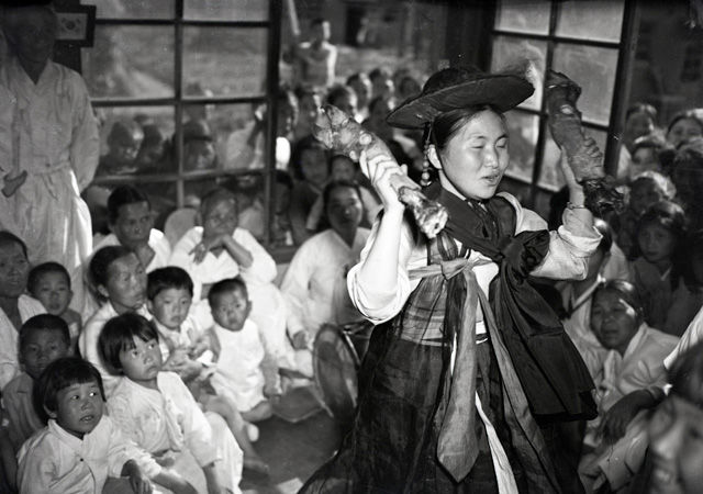 메인이미지  2 : 1948년 한 무녀가 양손에 돼지족발을 하나씩 들고 굿을 펼치고 있다. 동네 꼬마 녀석들과 부녀자들이 빽빽하게 모여 앉아 굿 구경을 하고 있다. 이 사진은 당시 국내에 있던 한 미군이 촬영한 것으로 김한근 부경근대사료연구소 소장이 미국의 한 수집가로부터 입수했다. << 부경근대사료연구소 제공 >> (부산=연합뉴스)