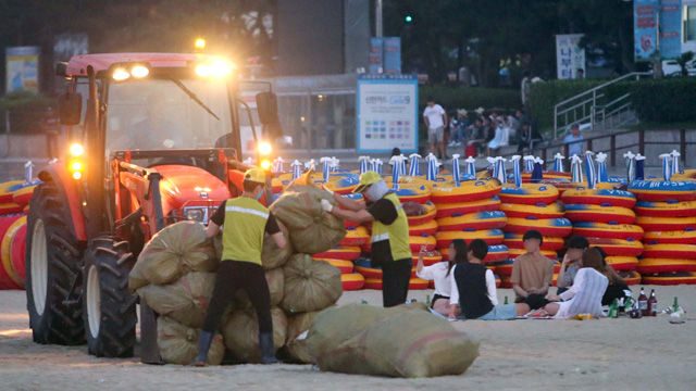 메인이미지  3 : 3일 오전 부산 해운대해수욕장 백사장에서 미화원들이 쓰레기를 수거하는 가운데 일부 피서객들이 새벽까지 술판을 벌이고 있다. 8월 첫 주말 해운대에는 170만명이 몰려 피서 절정을 맞았으나 피서객들이 마구 버린 쓰레기도 많았다. (부산=연합뉴스)