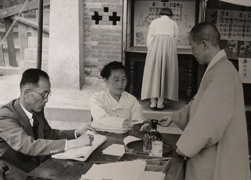메인이미지  6 : 1948년 5월 10일 신분을 확인하고 빈 투표용지를 받는 유권자. 뒤편의 여성은 투표용지를 작성하고 있다. (국사편찬위원회 제공)