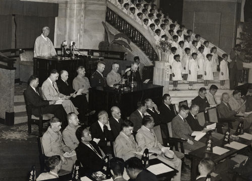 메인이미지  11 : 1948년 5월 31일 첫 국회 개회에 앞서 개회사를 하는 이승만 박사. 이승만 박사 앞에 앉은 6명의 외국인은 좌측부터 (한사람 건너뛰고) 경제고문 번스, 정치고문 제이콥스, 주한미군사령부 사령관 하지 중장, 군정장관 딘 소장, 군정장관대리 헬믹 소장, 교황사절 몬시뇨르 패트릭 번스 주교. (국사편찬위원회 제공)