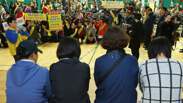 메인이미지  4 :  장애인 가족들(앞쪽)이 단상에서 무릎을 꿇고 공청회 시작과 시설물 건립을 호소하자 이에 설립을 반대하는 주민들이 무릎을 꿇고 자신들의 입장을 이야기하고 있다.
