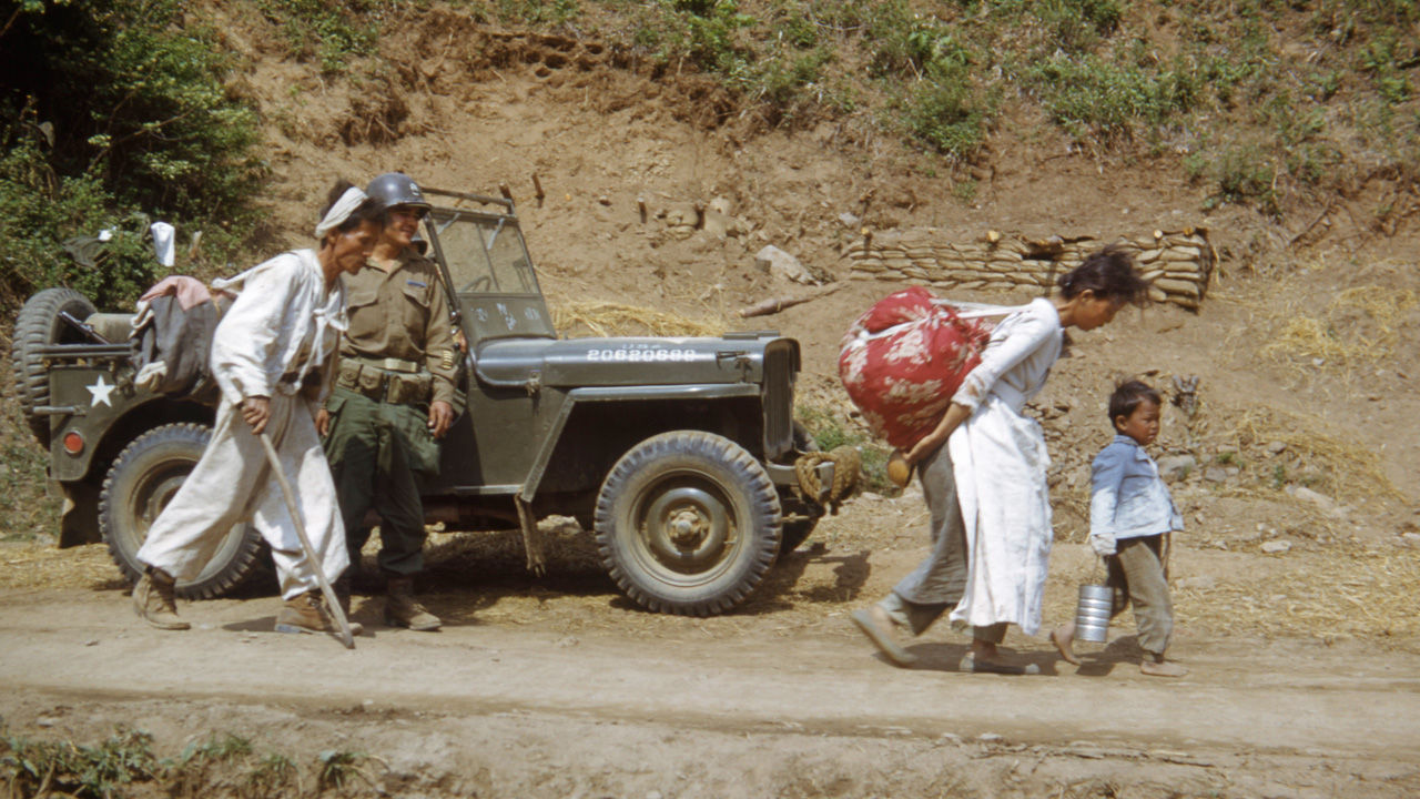 1951년 2월경 도로변 진지 앞에 세워진 미군 지프 차량 옆을 지나는 피란민 가족