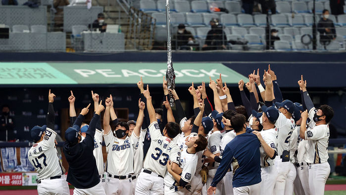 메인이미지  3 : NC 다이노스 선수들이 그라운드에서 모기업 NC소프트의 온라인게임 리니지의 집행검을 들어올리며 승리를 자축하고 있다.