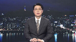 안경을 쓴 남성 뉴스 앵커가 밤의 서울 야경을 배경으로 스튜디오에 앉아 있다.