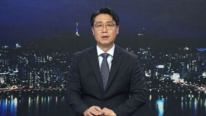 안경을 쓴 남성 뉴스 앵커가 서울 야경을 배경으로 정면을 응시하고 있다.