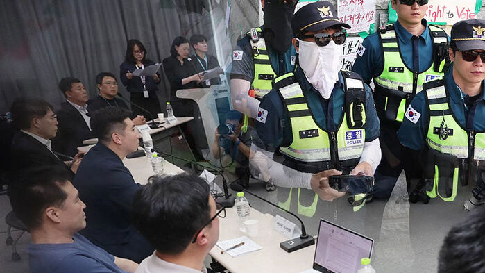 경찰 제복을 입고 마스크를 쓴 경찰관들이 기자회견장 옆에 서 있는 모습.