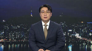 안경을 쓴 남성 앵커가 밤의 서울 야경을 배경으로 뉴스를 진행하고 있다.