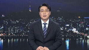 안경을 쓴 남성 앵커가 정장을 입고 야경을 배경으로 뉴스를 진행하고 있음.