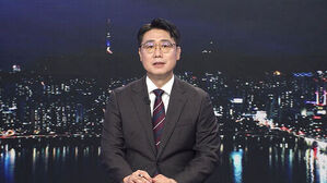 야간 서울 도심 배경 앞에 정장 차림의 남성 앵커가 앉아 뉴스를 진행하고 있다.