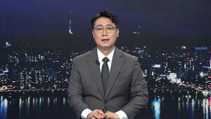 안경을 쓴 남성 앵커가 정장 차림으로 야경 배경의 뉴스 스튜디오에 앉아 있다.