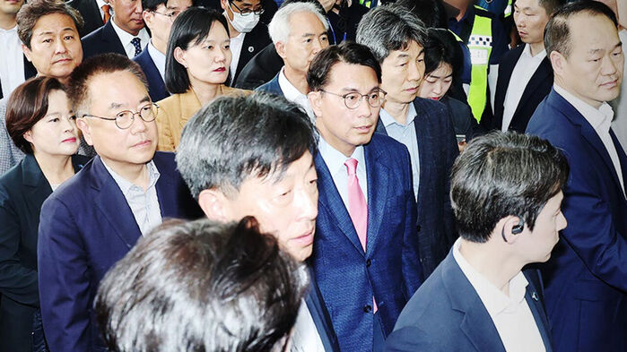 정장 차림의 남녀 다수가 진지한 표정으로 함께 이동하는 모습.