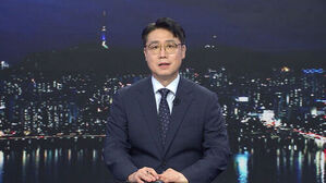 안경을 쓴 남성 앵커가 정장을 입고 뉴스 스튜디오에 앉아 있는 모습. 배경은 서울 야경.