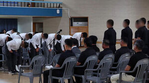 흰 셔츠를 입은 사람들이 고개 숙여 인사하고, 검은 옷을 입은 사람들이 앉아서 이를 지켜보는 모습.