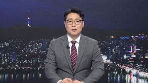 안경을 쓴 남성 앵커가 정장을 입고 야경 배경 앞에서 뉴스를 진행하고 있다.