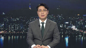 안경을 쓴 남성 뉴스 앵커가 정장을 입고 서울 야경 배경 앞에서 소식을 전하고 있다.