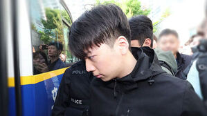 경찰 호송차 앞에서 검은 옷을 입은 남성이 고개를 숙인 채 이동하고 있다.