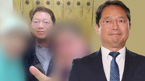 안경을 쓰고 정장 차림을 한 남성의 모습과 배경에 흐리게 처리된 인물 사진