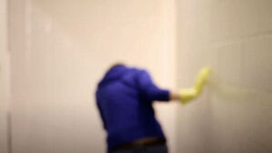 노란 고무장갑을 끼고 타일 벽을 닦는 사람의 뒷모습