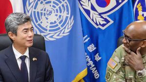 UN기와 태극기 배경 앞에서 대화하는 정장 차림의 한국인 남성과 군복 차림의 외국인 남성