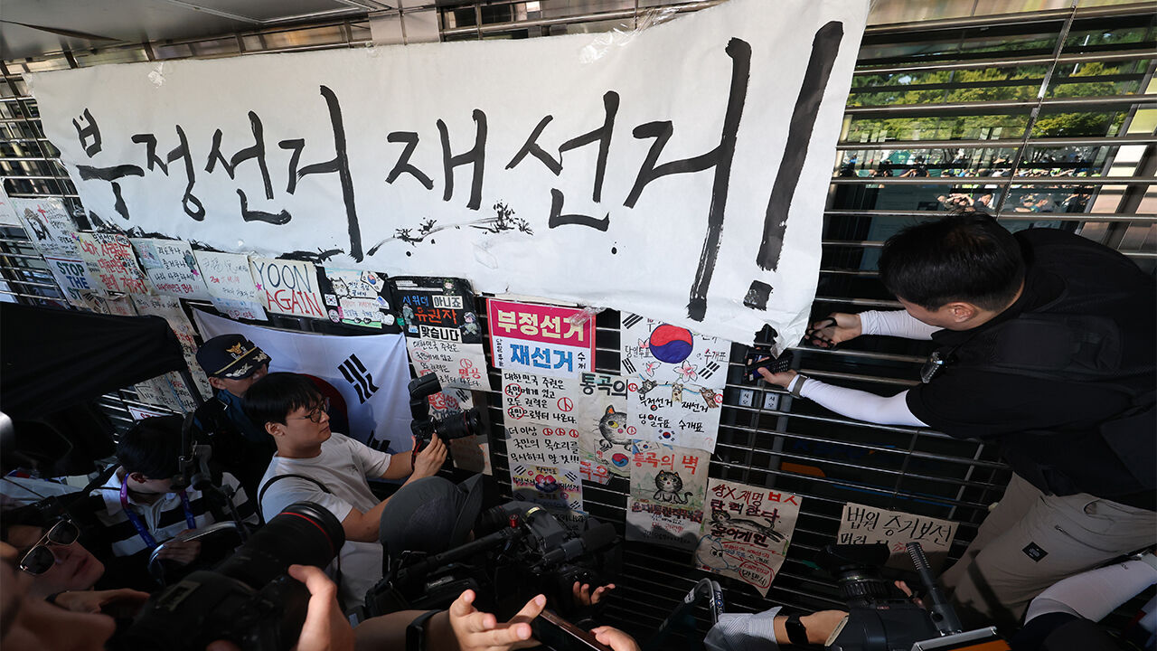 6·3 지방선거 투표용지 부족 사태로 촉발된 잠실 개표소 봉쇄 시위가 이어진 지난달 8일 서울 송파구 올림픽공원 핸드볼경기장에서 경찰이 진입을 위해 '부정선거 재선거'라는 문구가 적힌 종이를 제거하고 있다.